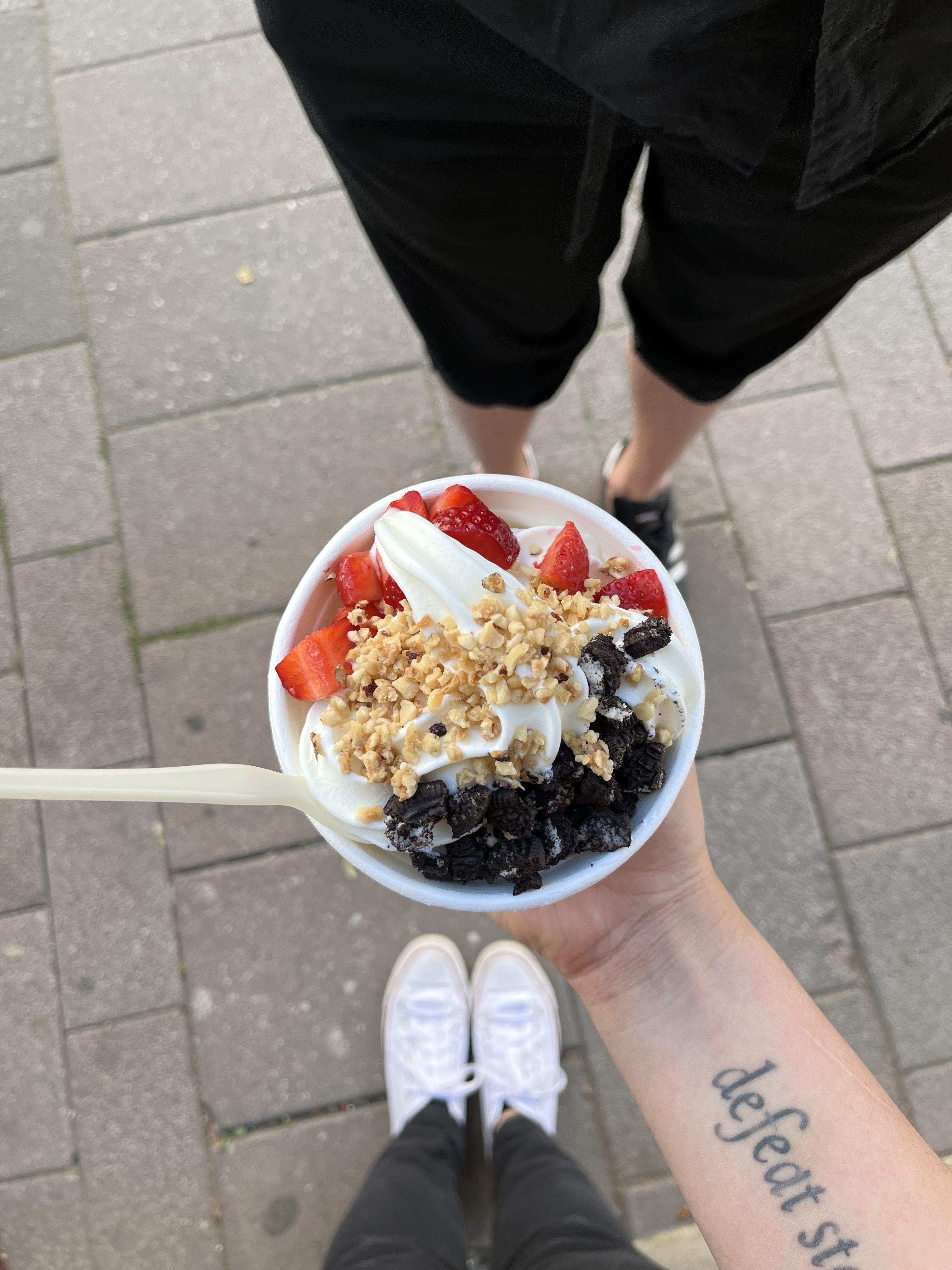 Holding a cup of frozen yogurt topped with Oreo cookie crumbs, cut strawberries and almond crunch